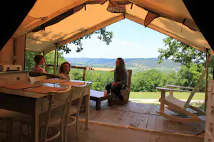 Blick von der Zelt-Terrasse auf eine Küche mit Tisch und Stühlen sowie auf das Tal und die Bäume im Hintergrund.