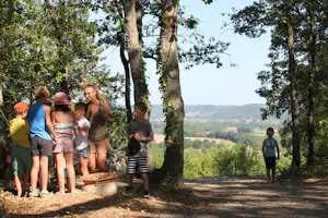 Familie steht am Weg im Wald, Kinder und Erwachsene schauen auf einen kleinen Brunnen neben dem Pfad.
