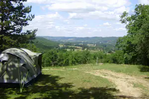 Campingzelt auf einer Wiese am Hang, umgeben von Bäumen, mit weitem Blick ins grüne Tal.