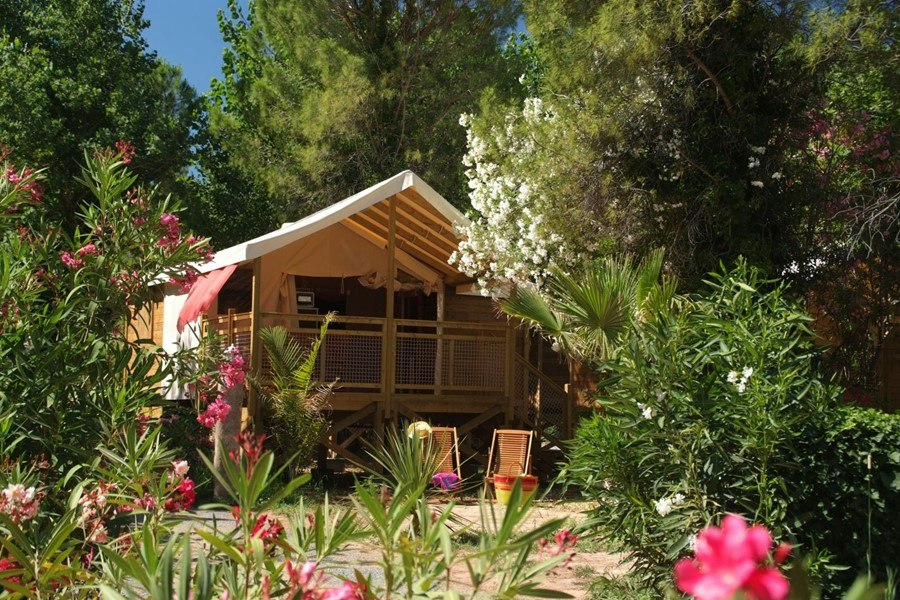 Campingzelt auf einer Stellfläche mit Holzpodest, umgeben von Büschen und bunten Blumen im Grünen.