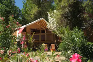 Campingzelt auf einer Stellfläche mit Holzpodest, umgeben von Büschen und bunten Blumen im Grünen.