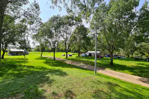 Campingplatz mit grünem Rasen, Zelt und Wohnwagen, Autos am Wegesrand und Bäumen entlang der Stellplätze.