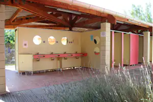 Überdachte Camping-Küchenzeile mit Spülbecken, Wasserhähnen und Fliesenboden, daneben mehrere Schränke unter Holzdecke.