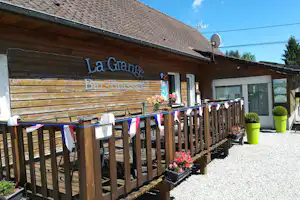 La Grange Bar-Brasserie mit Holzfassade, Terrasse und Tischen vor dem Eingang, Sonnenschirme und Deko-Wimpel.