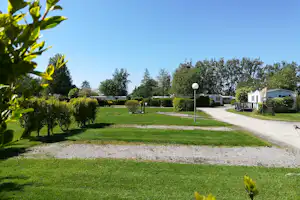 Grüne Campinganlage mit Rasen, Kiesweg und Reihen von Mobilheimen, umgeben von Hecken und Bäumen.