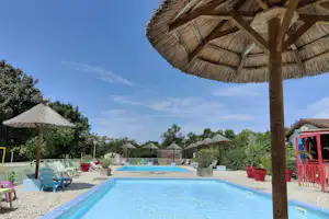 Blick auf den Camping-Pool mit Sonnenschirmen, Liegen und einem Holz-Pavillon am Beckenrand.