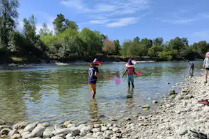 Menschen paddeln mit Paddeln auf dem Fluss, im Vordergrund Kiesufer und Steine am Ufer.