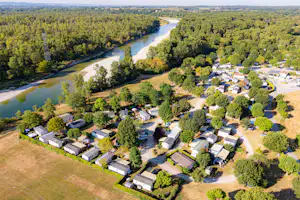 Luftaufnahme eines Campingplatzes mit Wohnwagen und Zelten, Wegen und Bäumen, am Fluss mit grünen Ufern.