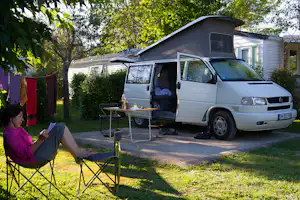 Weißes Wohnmobil am Campingplatz mit ausgeklapptem Vorzelt, Tisch und Campingstühlen im Garten neben einem Baum.