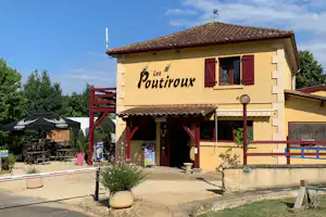 Gelbes Gebäude mit rotem Dach und Terrasse, Schild „Les Poutiroux“, davor Weg und Sitzbank im Campingbereich.
