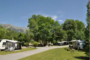 Campingplatz mit Wohnmobilen und Vorzelten auf einem gepflegten Rasen, gepflasterter Weg und Bäume im Hintergrund.