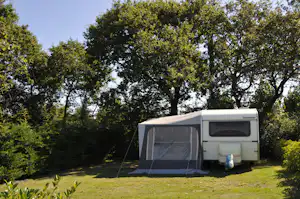 Wohnwagen mit Vorzelt auf einem Campingplatz, umgeben von Rasen und Bäumen im Hintergrund.