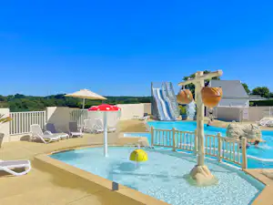 Schwimmbad mit Kinderbecken, Rutsche und Liegestühlen auf einer Terrasse, im Hintergrund Bäume und Hügel.