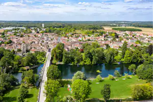 Blick auf einen See mit Ufergrün, dahinter eine Stadt und ein Flusslauf zwischen Bäumen und Häusern.