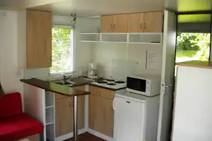 Küchenzeile im Camping-Unterkunftsraum mit Spüle, Herdplatten, Mikrowelle und Kühlschrank, Blick auf Fenster mit Jalousien.