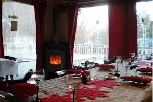 Gedeckter Tisch mit roten Servietten und Gläsern, im Hintergrund Kamin mit Flammen und Blick auf den Balkon.