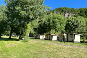 Reihe von Mobilheimen auf einem Campingplatz, umgeben von Rasen und hohen Bäumen, mit Kiesweg im Vordergrund.