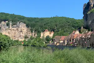 Blick vom Campingplatz auf einen Fluss, Wiesen und die Altstadt mit Häusern am Hang unter Felsen.