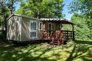 Holz- und Metall-Campingunterkunft mit Veranda und Stufen, umgeben von Bäumen und Rasen im Grünen.