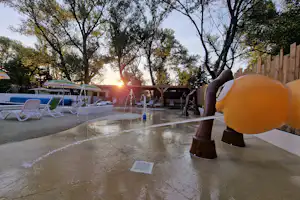 Terrasse am Campingplatz mit Sitzbank, Flaschen auf dem Tisch, Bäumen und Sonnenuntergang im Hintergrund.