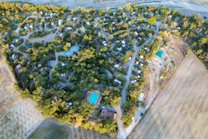 Luftaufnahme eines Campingplatzes mit vielen Stellplätzen, Wohnmobilen, Bäumen und einem blauen Pool im Gelände.