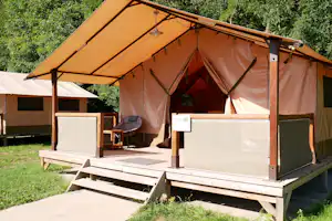 Glamping-Zelt mit Holzterrasse, Sitzbank und Sonnenschirm im Grünen, daneben ein weiterer Wohnbereich mit Markise.