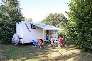 Weißes Wohnmobil mit Markise auf einem Campingplatz, daneben Campingstühle und Kinderfahrräder im Grünen.