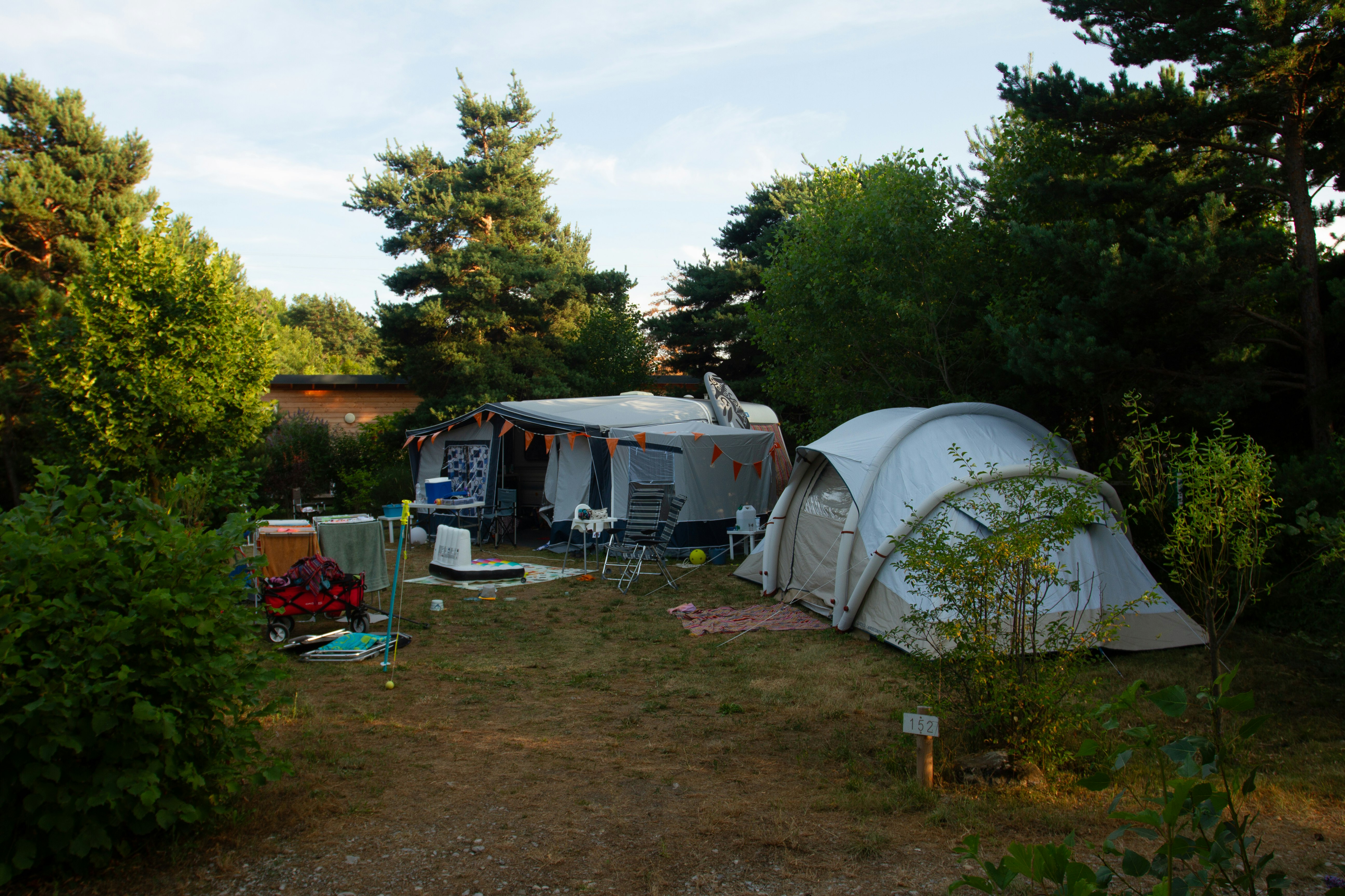 Zwei Campingzelte auf einem Grasplatz, daneben Campingstühle und ein kleines Vorzelt zwischen Bäumen.