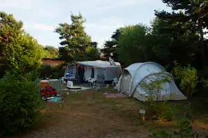 Zwei Campingzelte auf einem Grasplatz, daneben Campingstühle und ein kleines Vorzelt zwischen Bäumen.