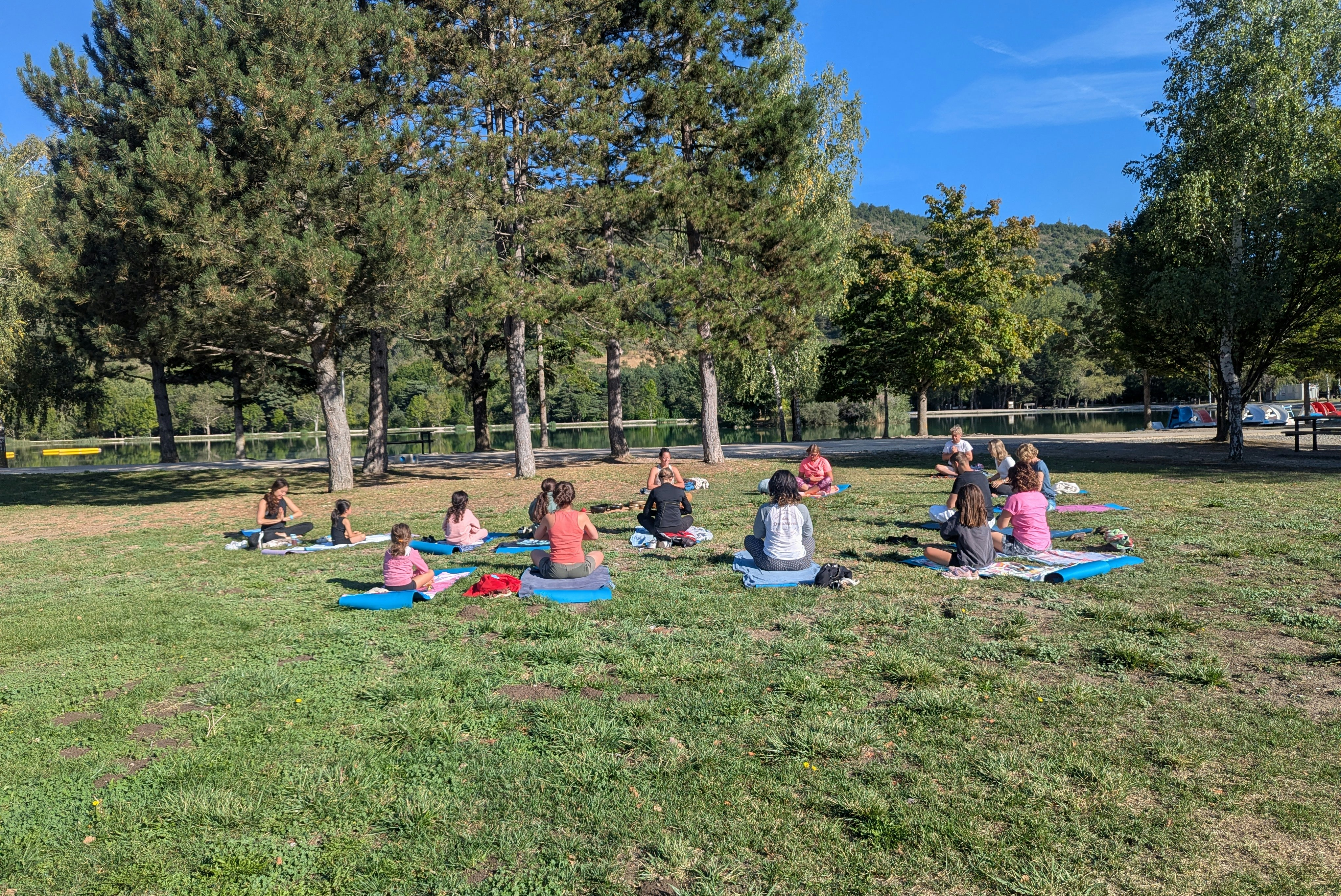 Yoga-Gruppe auf Matten im Grünen auf dem Campingplatz, umgeben von Bäumen und Rasenfläche.