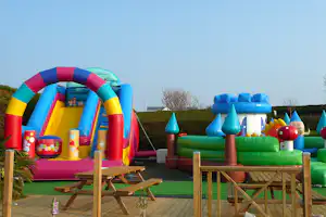 Aufblasbare Kinder-Spielanlage mit Rutsche, Kletterwand und bunten Hindernissen auf einer Camping-Terrasse.