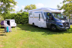 Wohnmobil mit Markise und Vorzelt auf dem Campingplatz, daneben Gartenmöbel und Tisch auf dem Rasen.