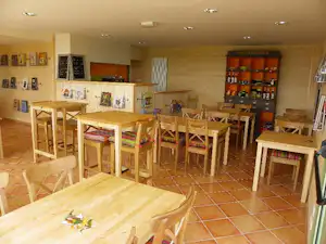 Innenbereich mit mehreren Holztischen und Stühlen, Fliesenboden und Getränkeschrank im Camping-Umfeld.