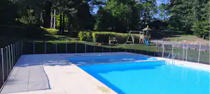 Camping-Pool mit blauem Wasser, Liegeflächen und Treppengeländer, umgeben von Bäumen und gepflegtem Grün.