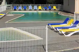 Schwimmbecken mit Holzumrandung und mehreren blauen und gelben Liegen auf dem Campingplatz, hinter einem weißen Zaun.