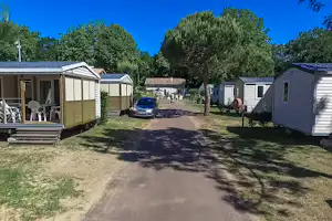 Reihe von Mobilheimen und Wohnwagen auf dem Campingplatz, mit Auto auf dem Weg und Bäumen im Hintergrund.