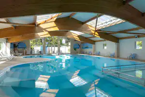 Innenpool mit blauem Wasser, Edelstahlgeländer und Liegen unter einem Glasdach im Campingbereich.