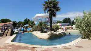 Schwimmbecken auf einem Campingplatz mit Palmen, Sonnenschirmen und Liegen, im Hintergrund ein weißes Runddach.