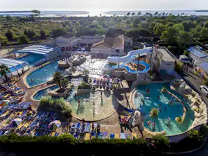 Großer Campingplatz mit mehreren Schwimmbecken, Sonnenliegen und Sonnenschirmen, umgeben von Bäumen und Ferienhäusern.
