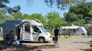 Wohnmobil auf dem Stellplatz, daneben Zelt und Fahrrad, im Hintergrund weitere Fahrzeuge und Bäume.
