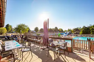 Terrasse am Campingplatz mit Tisch, Stühlen und Sonnenschirm, Blick auf den Pool und Liegen im Außenbereich.