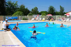 Großes Camping-Schwimmbecken mit Kindern im Wasser auf Schwimmhilfen, Liegen am Rand und Zaun im Hintergrund.