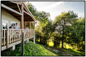 Camping Les Terrasses du Périgord - Gäste sitzen vor dem Mobilheim im Schatten der Bäume auf dem Campingplatz