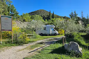 Wohnmobil auf Stellplatz am Campingplatz, Schotterweg, Hecken und Bäume, im Hintergrund Hügel und Zypressen.