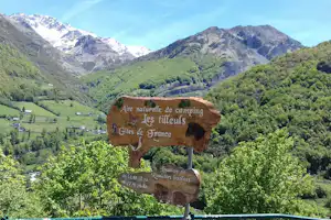 Schild „Les tilleuls“ am Campingplatz mit Blick ins grüne Tal und auf schneebedeckte Berge in den Pyrenäen.