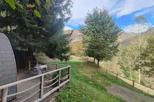 Stellplatz mit Terrasse und Geländer, Blick auf Wiese, Bäume und Berge im Hintergrund.