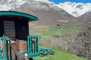 Balkon mit türkisfarbenem Geländer und Bank, Blick ins grüne Tal und auf schneebedeckte Berge.