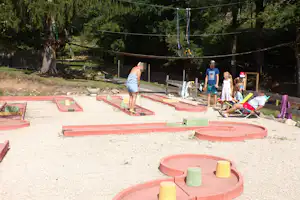 Minigolfanlage auf dem Campingplatz mit roten Bahnen, bunten Hindernissen und Sitzbereich im Grünen.