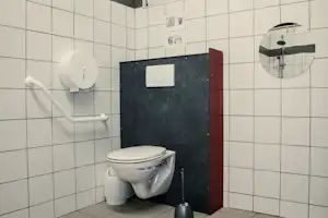 Toilette im Badezimmer mit weißen Fliesen, Spülkasten, Wandhalterung und Handtuchhalter.