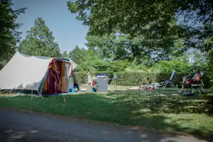 Campingzelt im Grünen mit Sitzbereich und Stühlen, daneben ein weiterer Zeltbereich und Bäume im Hintergrund.